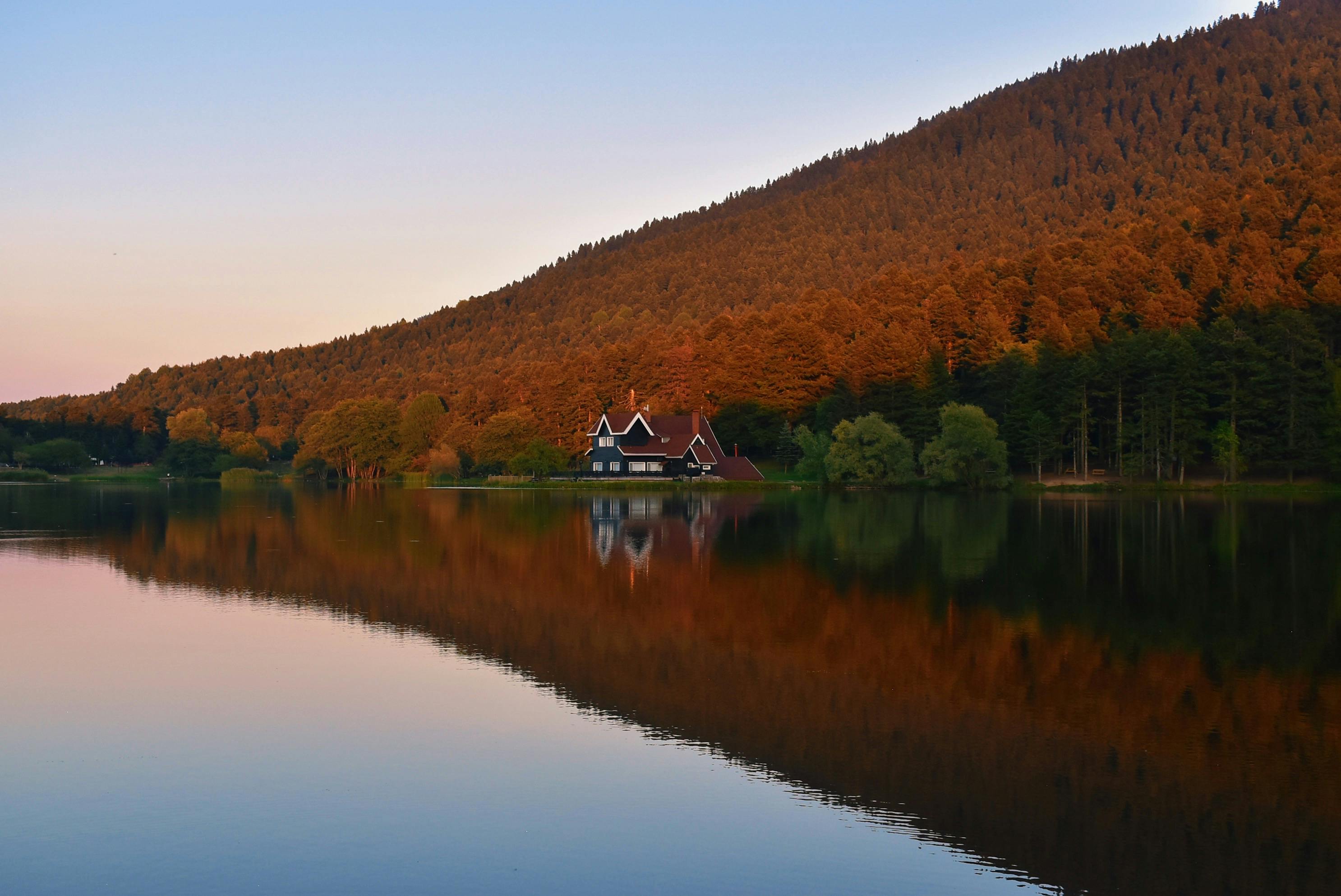 Beautiful lake house surrounded by autumn forest reflecting in water.