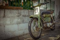 一辆经典的生锈绿色摩托车停在户外墙边，捕捉了老式交通的氛围