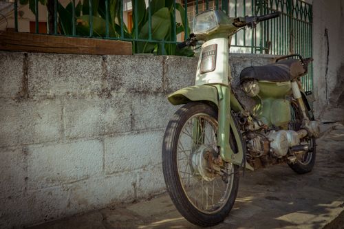 Free Classic rusty green motorcycle parked outdoors against a wall, capturing a vintage transportation vibe. Stock Photo