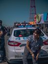 白天，在科尼岛，一名妇女靠在警车上，捕捉到了一幅坦率的街景