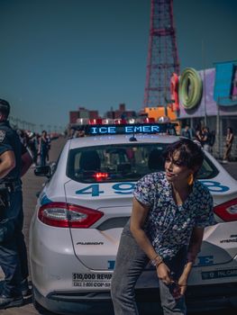 白天，在科尼岛，一名妇女靠在警车上，捕捉到了一幅坦率的街景