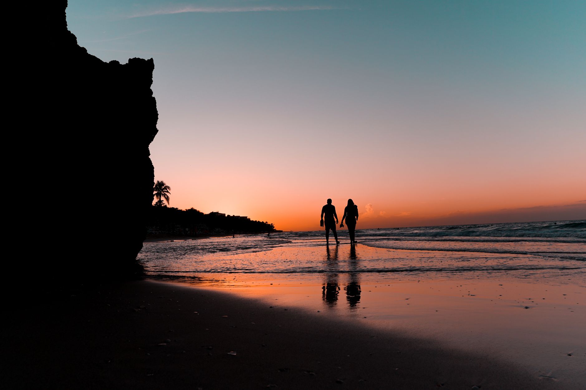 A couple walks hand in hand along Varadero Beach during a vibrant sunset.