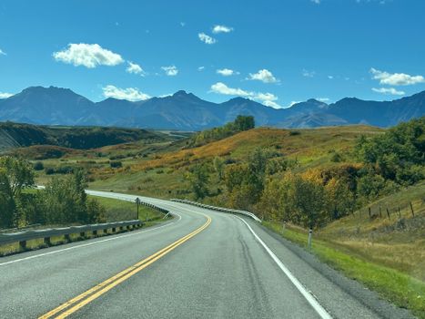 Winding road through a vibrant autumn landscape with mountains under a clear blue sky.