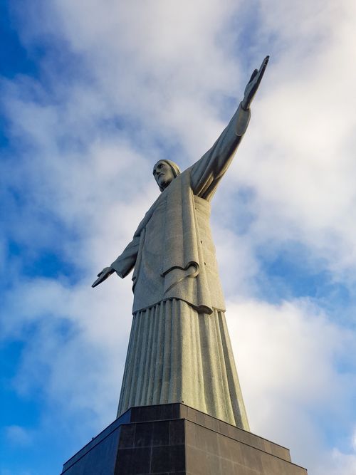 Free Christ the Redeemer statue against a blue sky with clouds, representing Rio de Janeiro's iconic landmark. Stock Photo