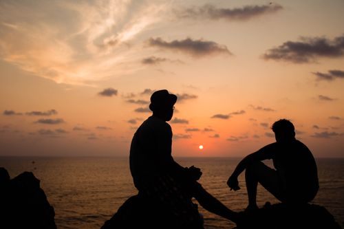 Free Two silhouetted figures sit against the vibrant sunset over the Arabian Sea in Chapora, Goa. Stock Photo