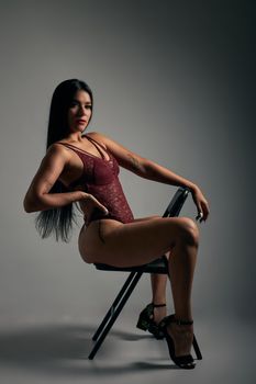 A confident woman in red lingerie and high heels posing on a chair, captured indoors.