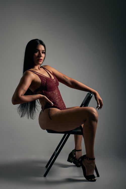 Free A confident woman in red lingerie and high heels posing on a chair, captured indoors. Stock Photo