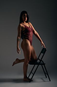 Elegant studio portrait of a woman posing in a burgundy lace bodysuit with moody lighting.