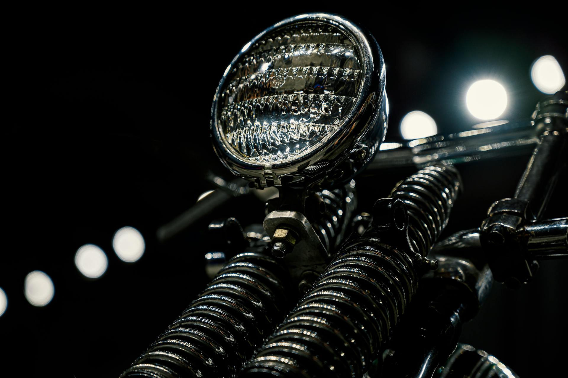 Close-up of a vintage motorcycle headlight with chrome detailing in low light.