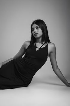 Elegant black and white portrait of a young woman in a relaxed pose, exuding confidence.