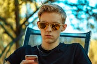 一名戴着太阳镜的年轻人在户外一边用智能手机放松身心