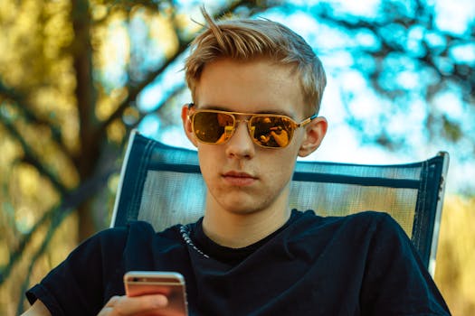 一名戴着太阳镜的年轻人在户外一边用智能手机放松身心