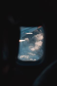 Looking through an airplane window at clouds and the wing, capturing the serenity of flight.