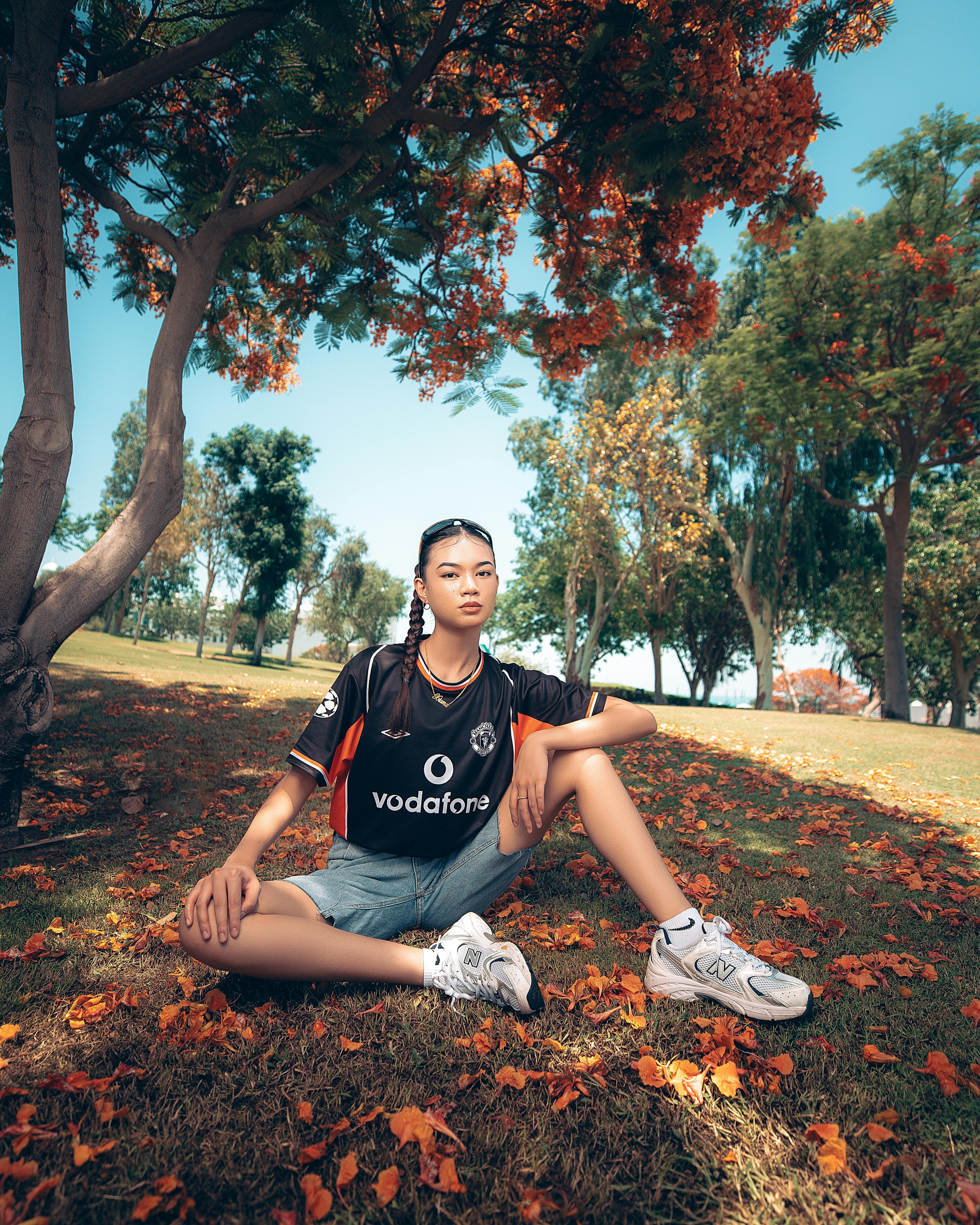 Young woman sits on grass amidst vibrant autumn foliage in a park setting.