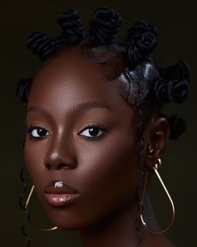 Elegant portrait of a woman with Bantu knots and gold earrings against a dark background.