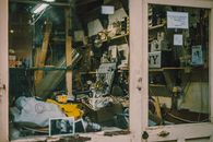A cluttered vintage workshop seen through a glass window, filled with tools and parts.