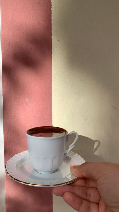 Free White coffee cup on a saucer held in front of a sunlit wall, creating a minimalist aesthetic. Stock Photo