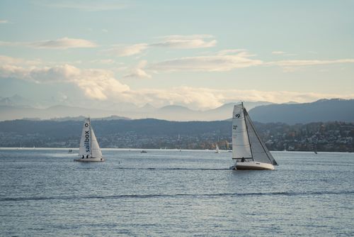 Free Sailboats gliding on a serene lake with picturesque mountain background under a gentle sky. Stock Photo
