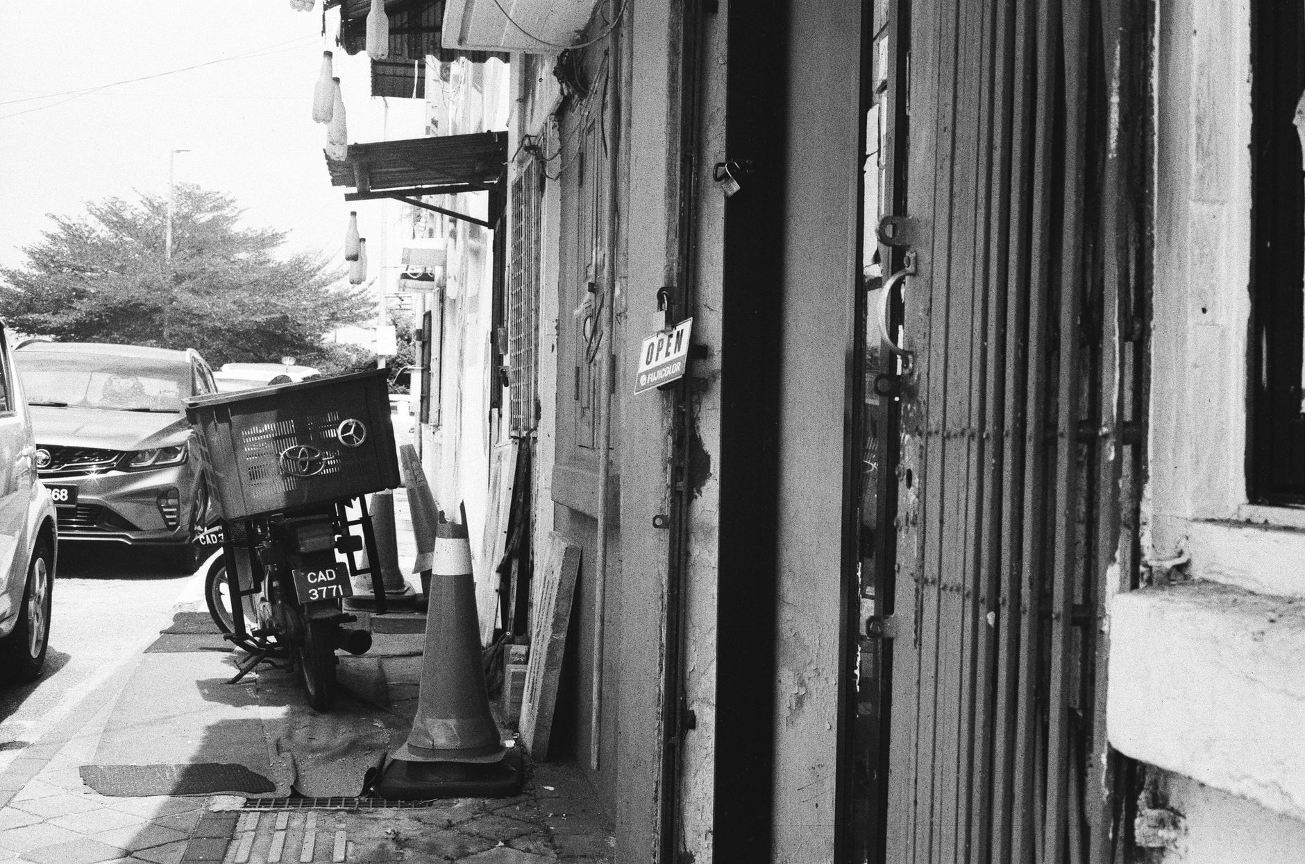 A classic street scene featuring a parked motorcycle, cars, and an open shop door.