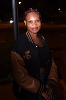 Portrait of a young woman smiling confidently in a nighttime urban setting.