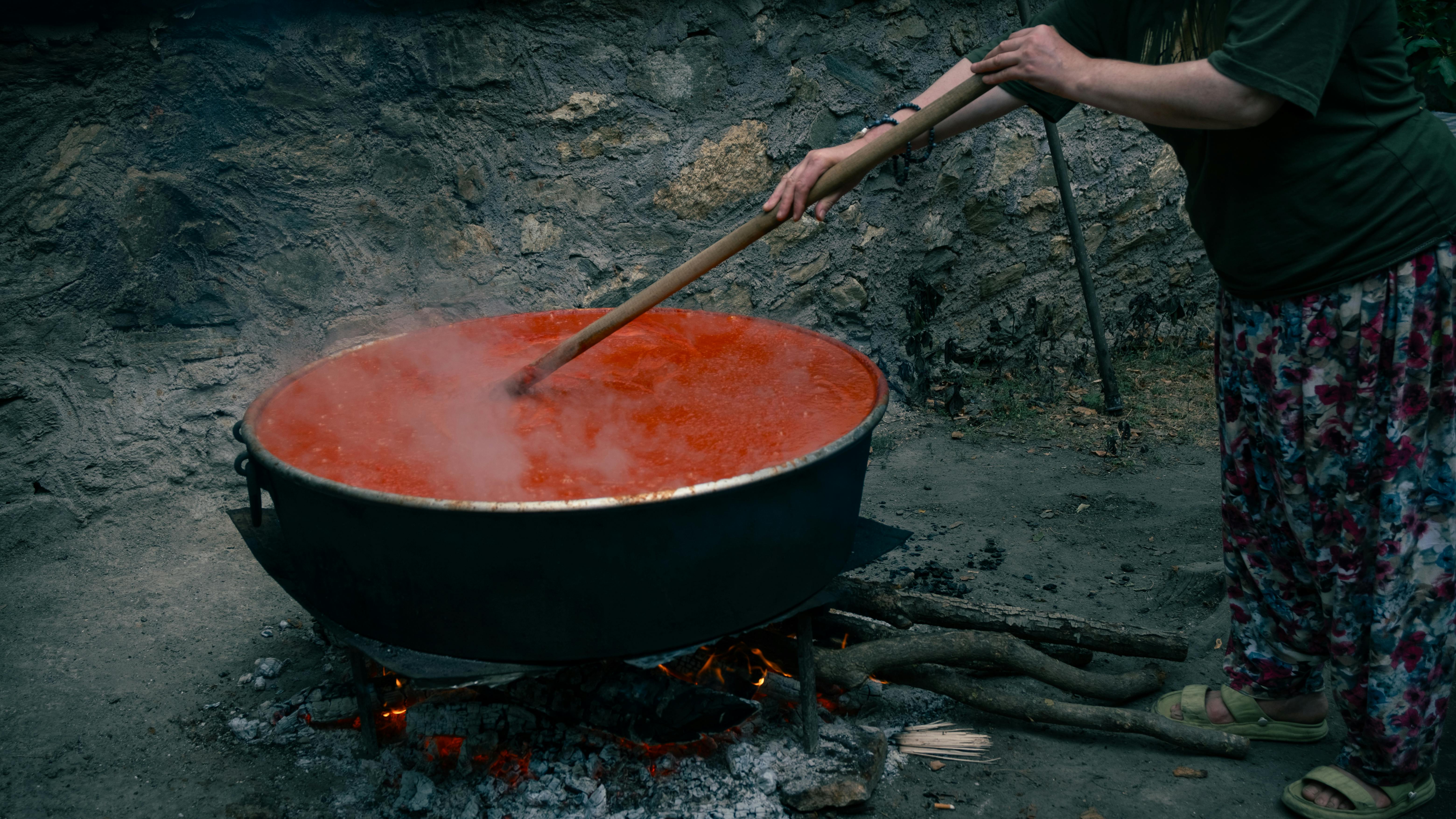 A woman stirring a large pot of boiling tomato paste outdoors in Bursa, Türkiye.
