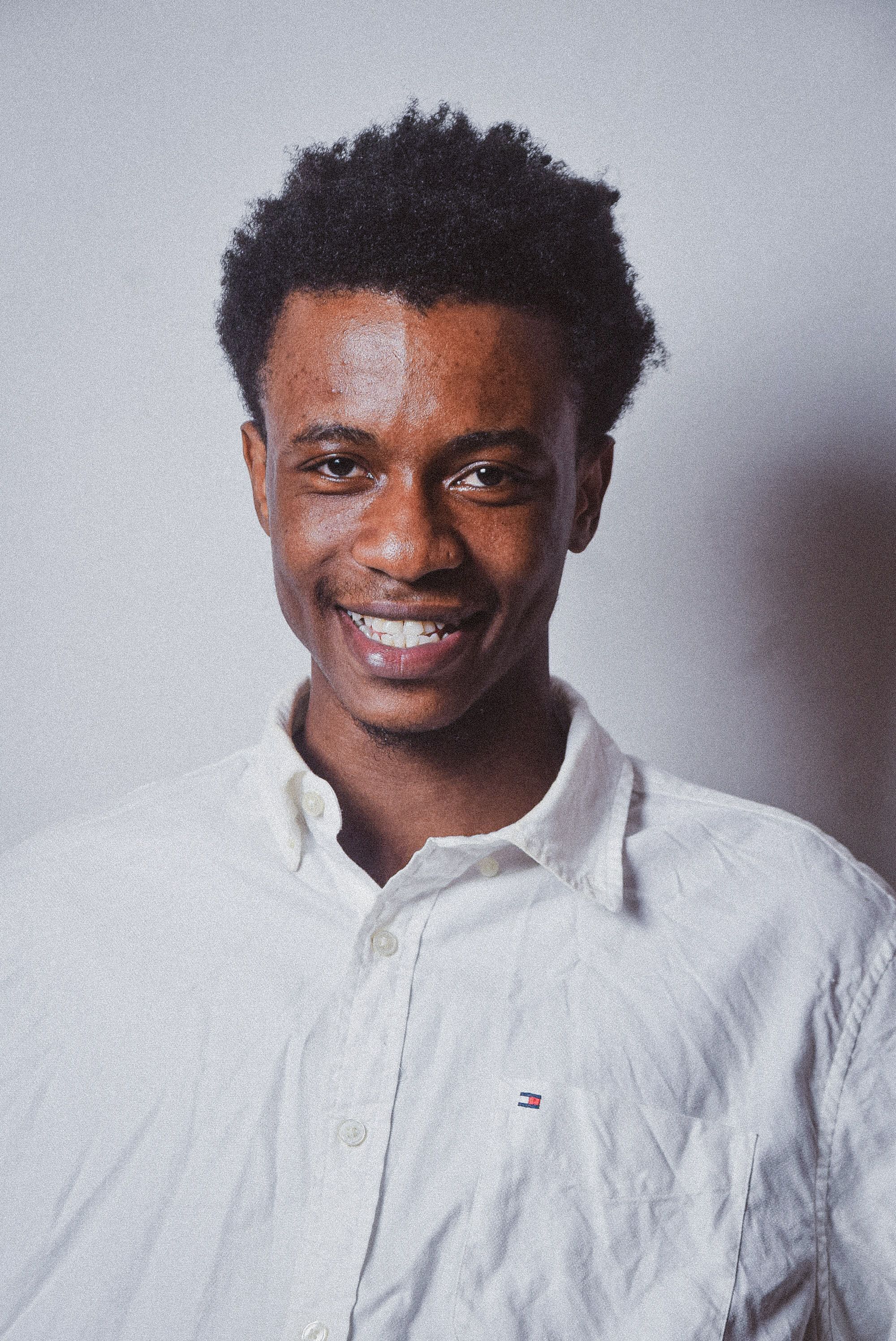 Portrait of a smiling young man in a white shirt against a plain background.