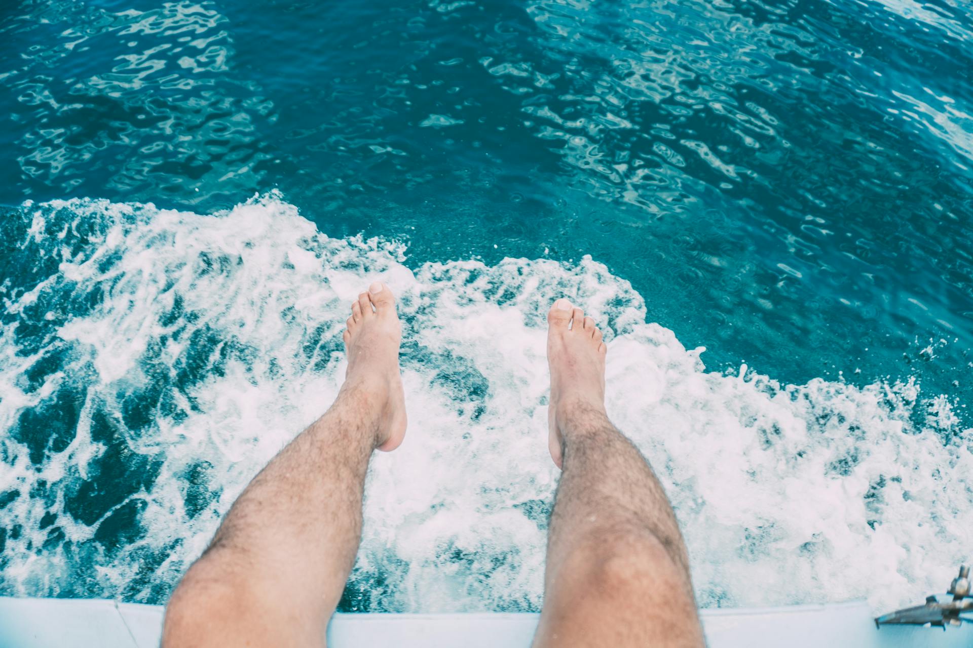 Feet dangling over a boat with ocean waves below, capturing a moment of relaxation.