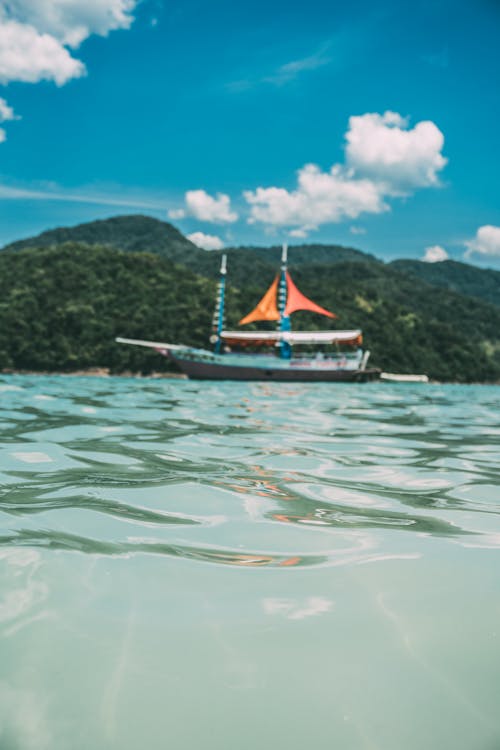 бесплатная черно оранжевая лодка возле зеленого острова Стоковое фото