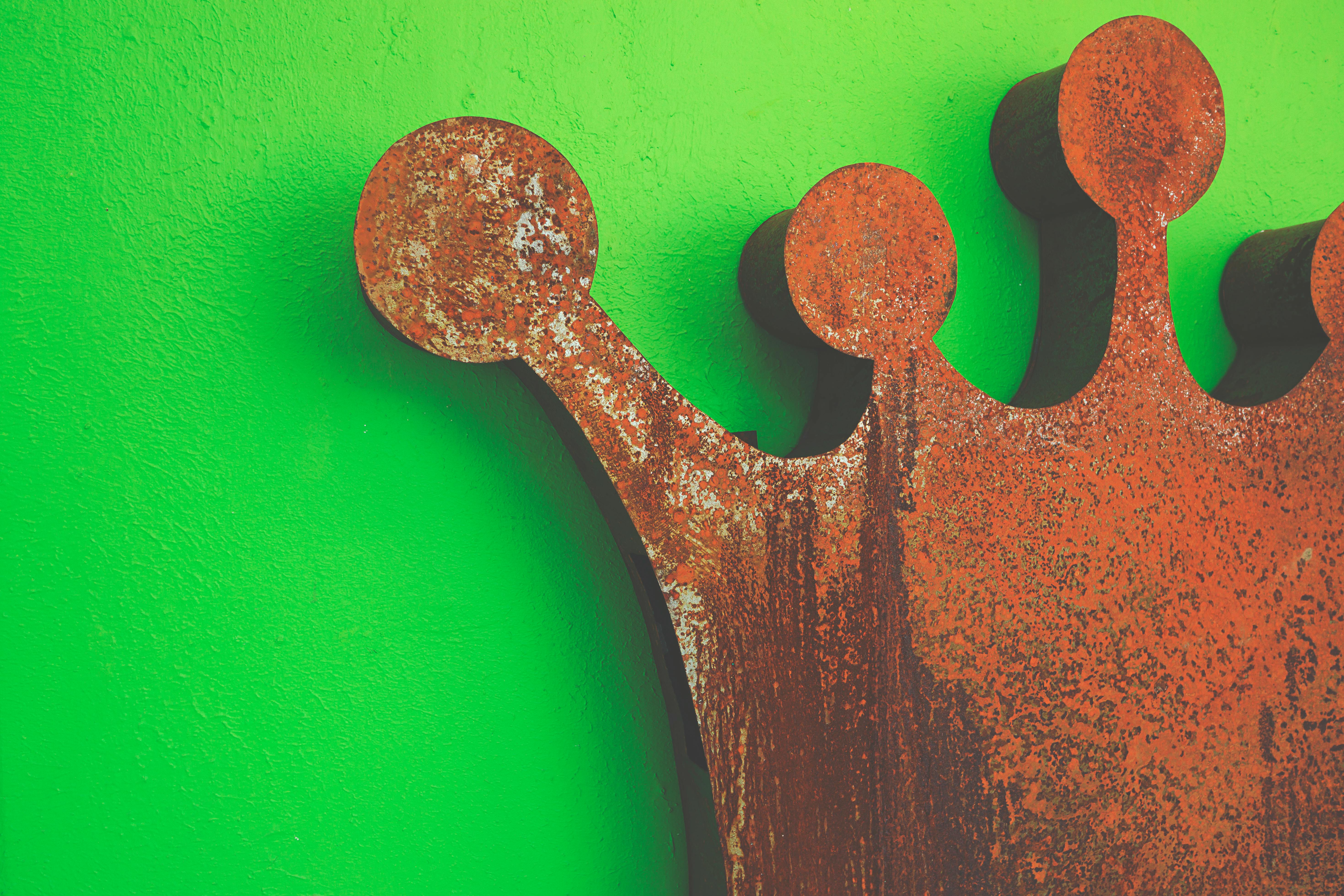 A rusty metallic crown against a green wall.