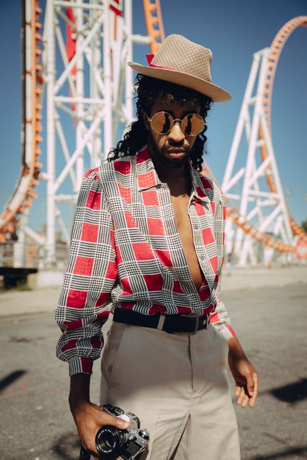 Stylish man in shades posing in front of roller coasters on a sunny day.