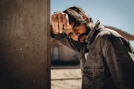 一名时尚男子穿着牛仔夹克，在户外的混凝土墙边摆出时尚的姿势