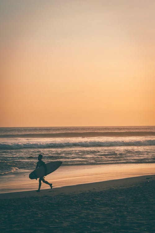 Мужчина несет доску для серфинга на берегу моря