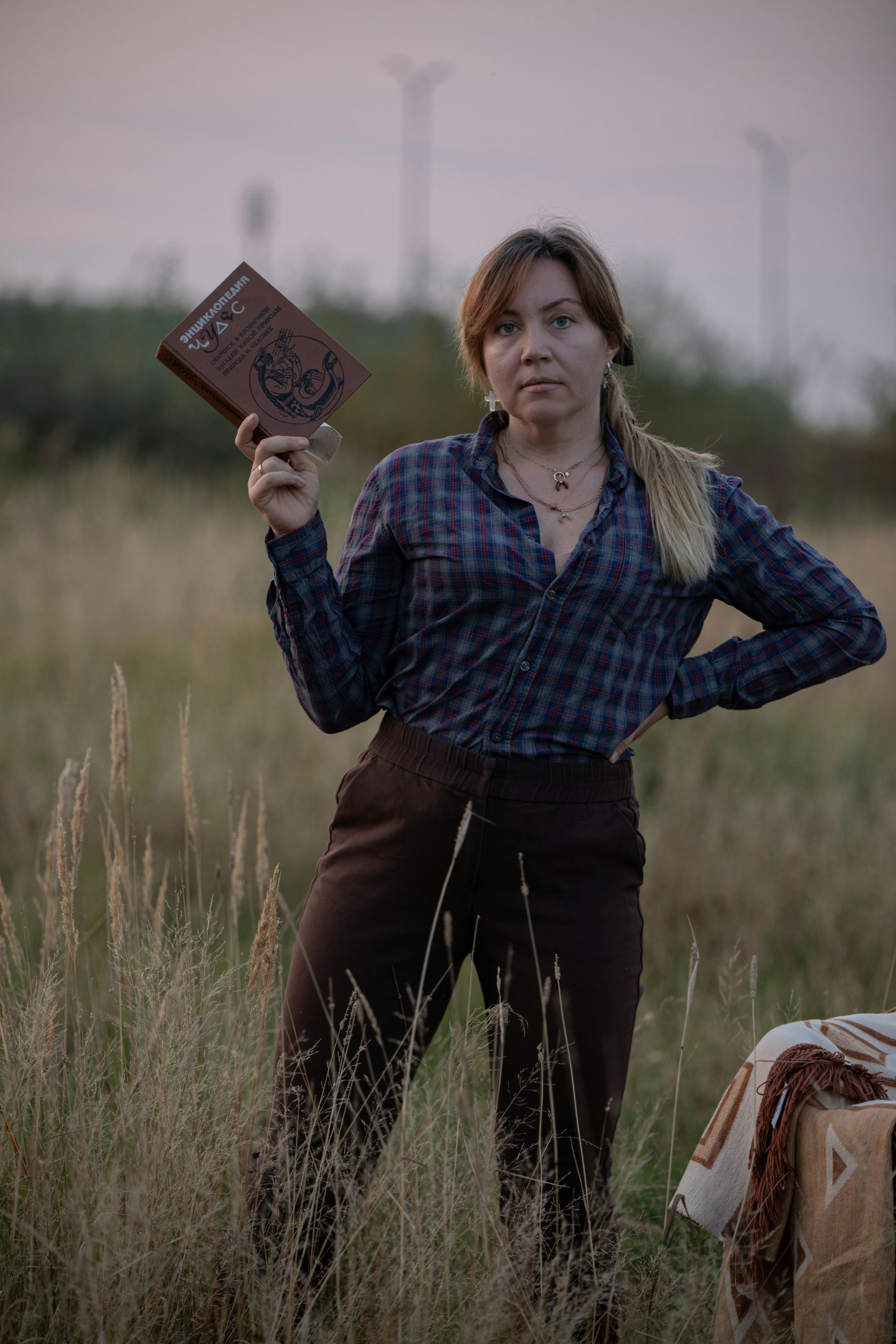 Woman standing in a field holding a book, showcasing determination and confidence at sunset.