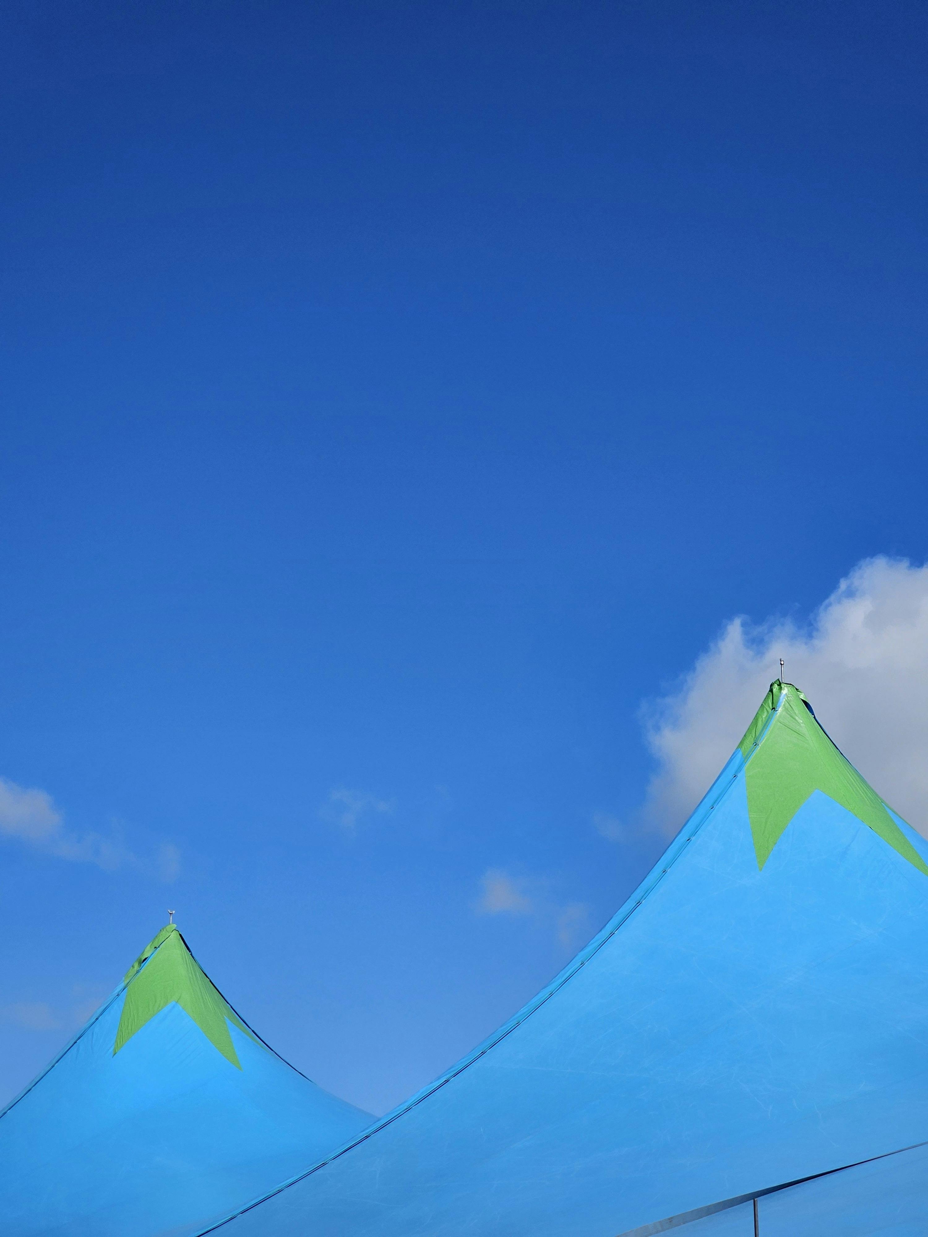 Bright blue and green tent tops under a vibrant sky with fluffy clouds.