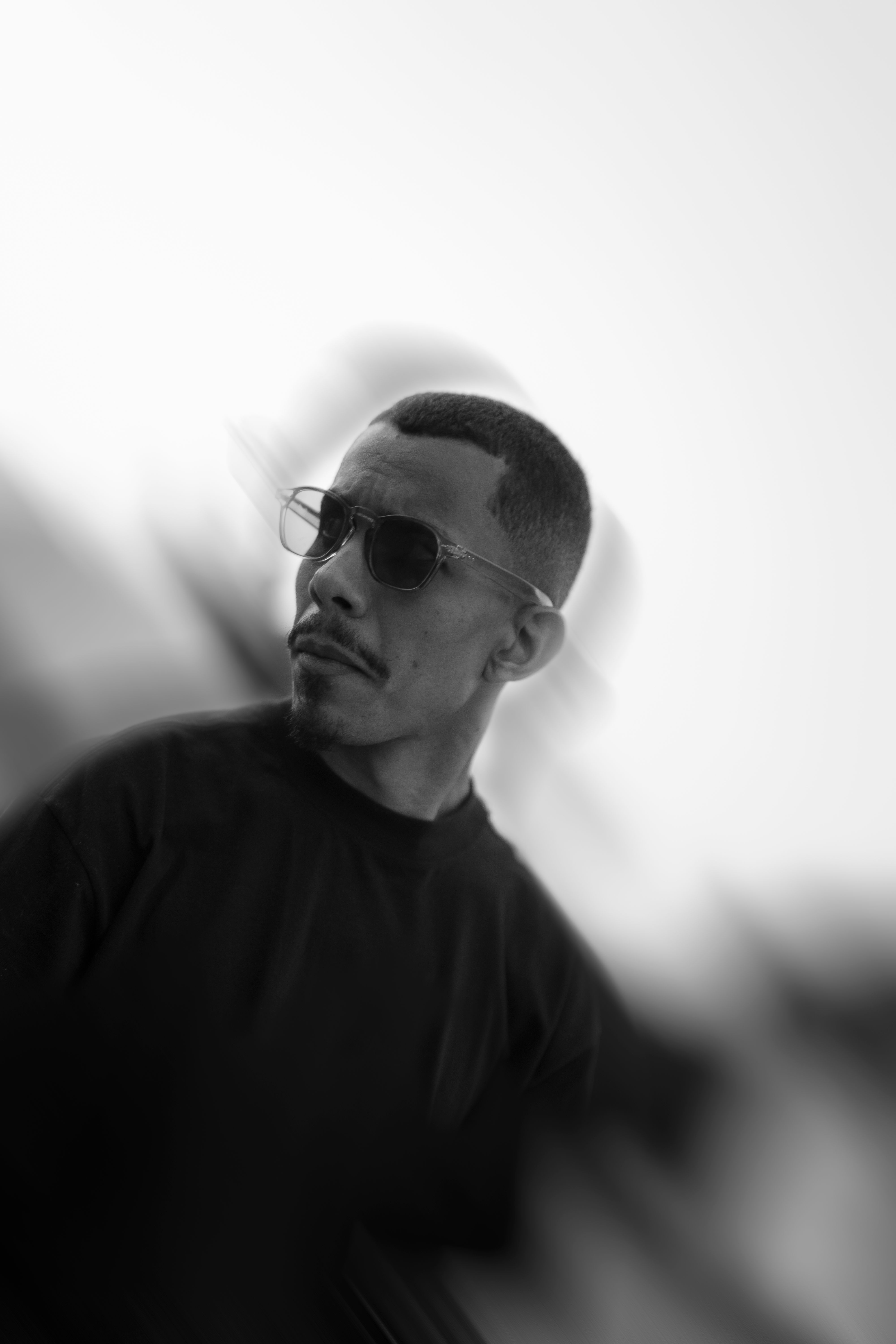 Stylish black and white portrait of a man wearing sunglasses with a blurred background.