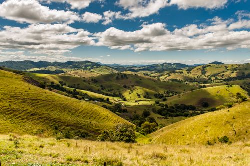 Free Stunning landscape of rolling hills and distant mountains under a bright blue sky with fluffy clouds. Stock Photo