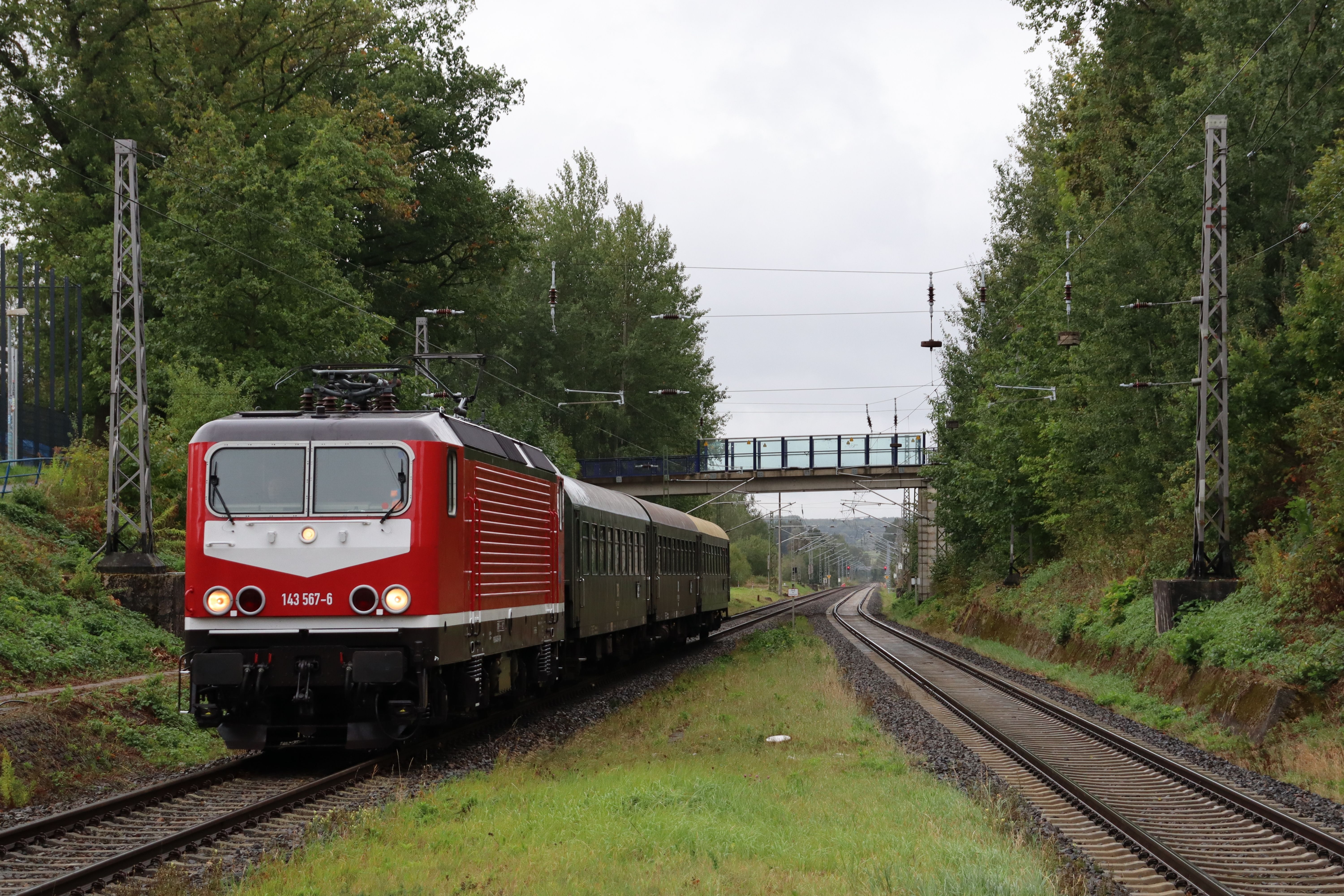 Red train traveling on tracks surrounded by greenery and an overpass bridge