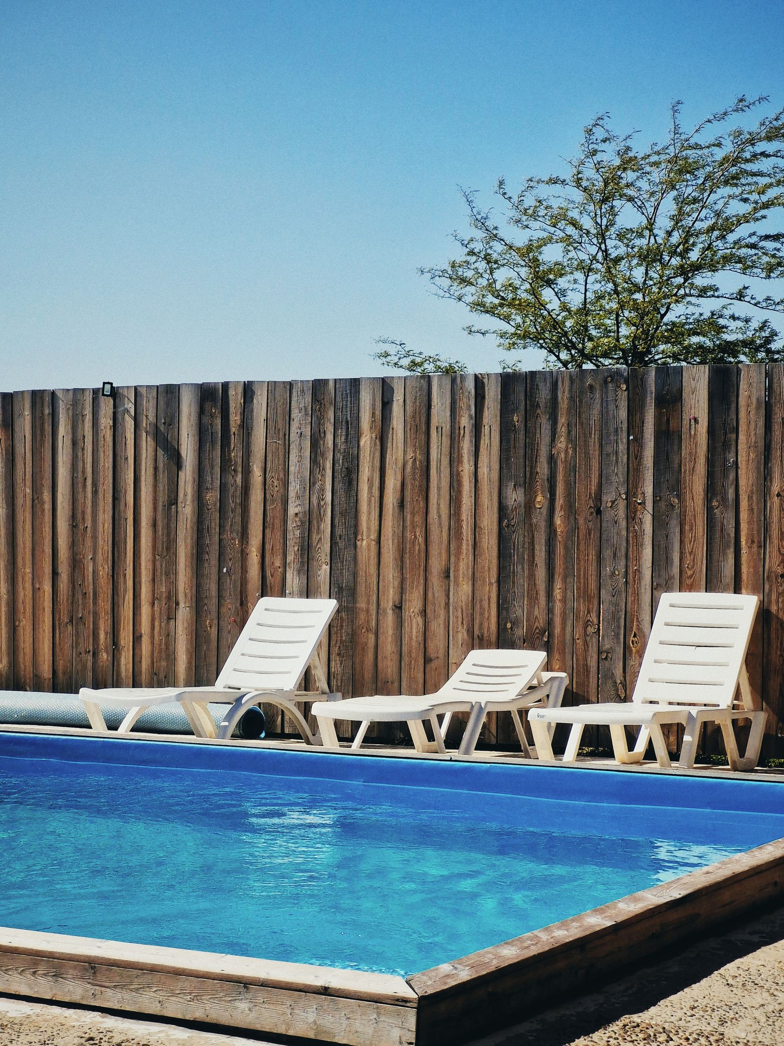 Piscina con zona de descanso junto a valla de madera