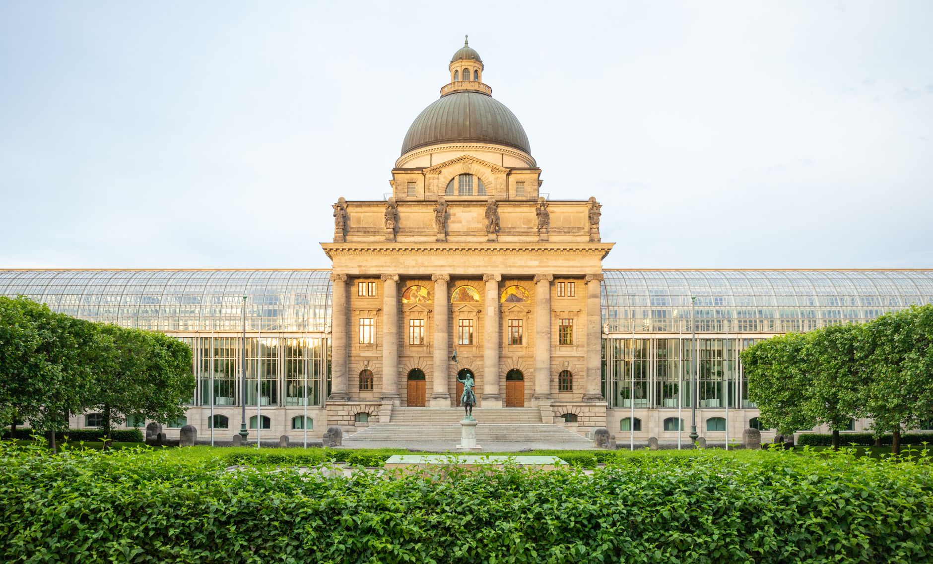 Front view of the Bavarian State Chancellery in Munich with lush gardens in the foreground.