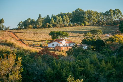Free A charming farmhouse in a serene rural setting surrounded by lush greenery under a clear sky. Stock Photo