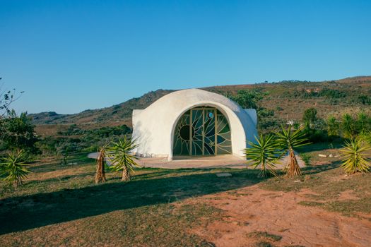 A white dome-shaped building set in a picturesque outdoor landscape under a clear blue sky.