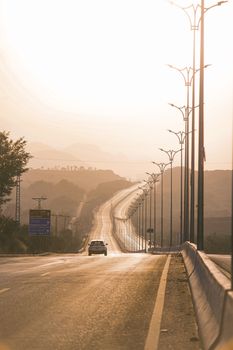 A solitary car drives on a deserted highway at sunset, creating a serene and isolated atmosphere.