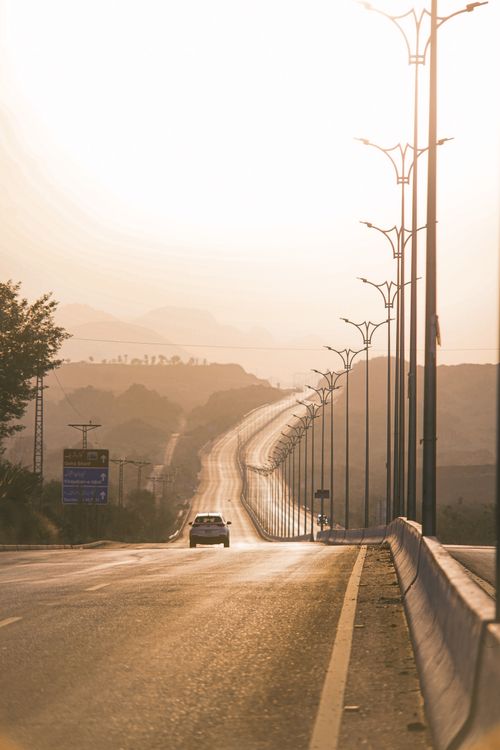 Free A solitary car drives on a deserted highway at sunset, creating a serene and isolated atmosphere. Stock Photo