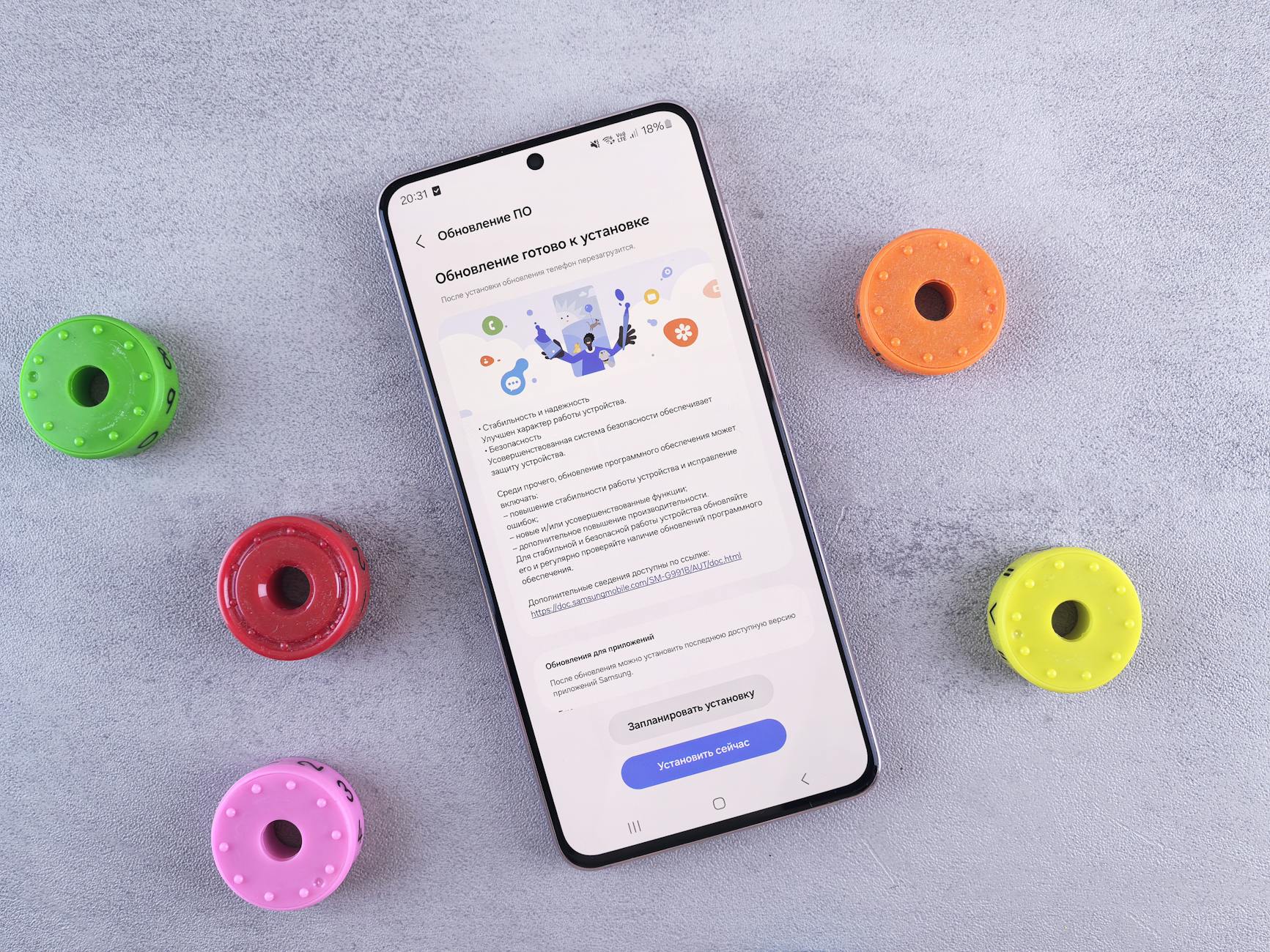 Flat lay of a smartphone displaying a software update, surrounded by colorful toy accessories on a gray desk.