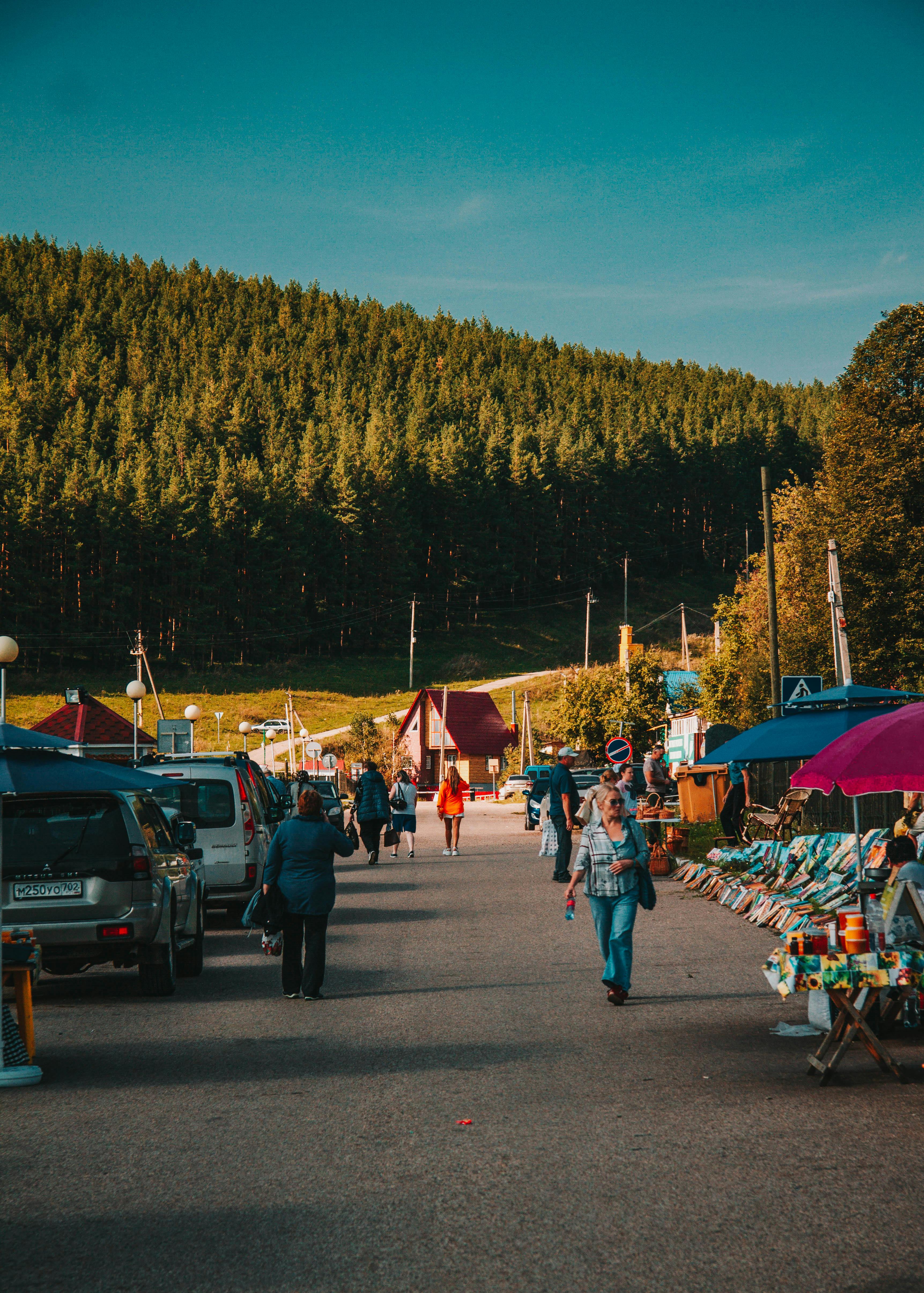 Charming market scene with people and stalls in a village against a lush forest backdrop in Bashkortostan.