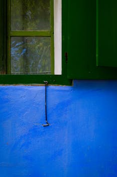 Close-up of a vibrant blue wall with an open green window and hook.