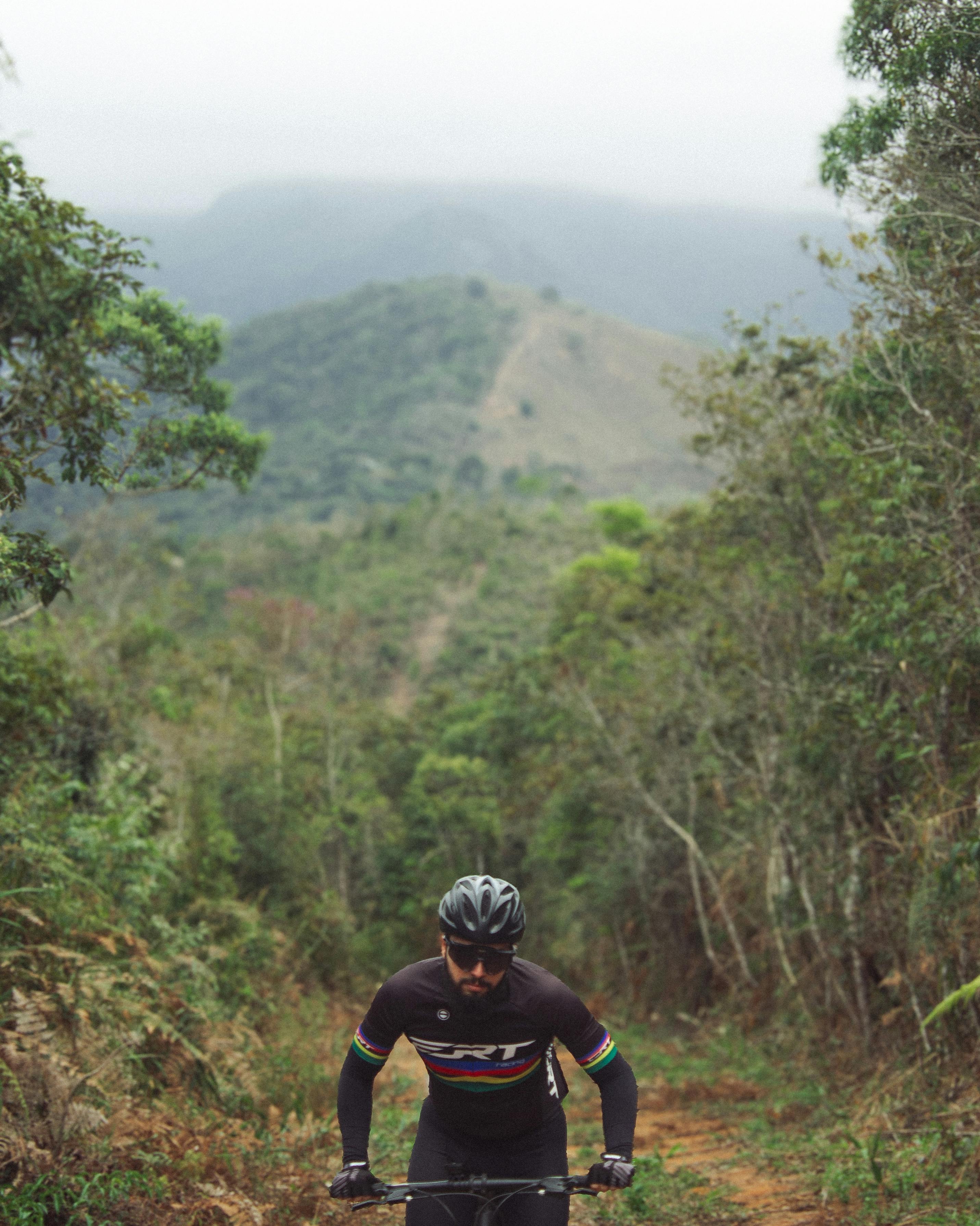 A cyclist wearing black gear enjoying a ride on lush green mountain trails.