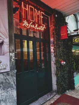 白天拍摄的城市旅馆入口，有红色霓虹灯标志和绿色的门，显得很温暖