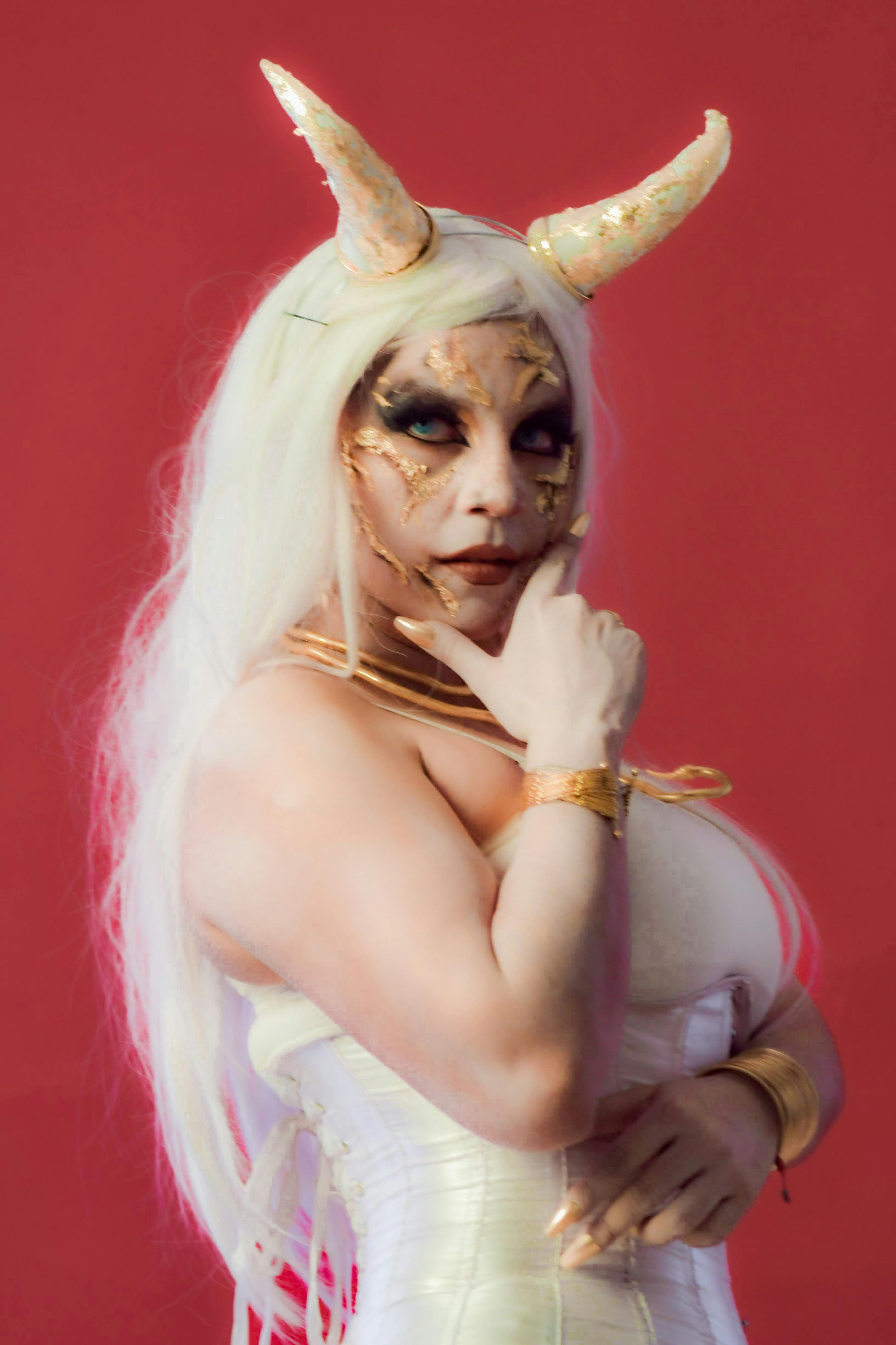 Woman in fantasy cosplay with horns and detailed makeup on a red background.