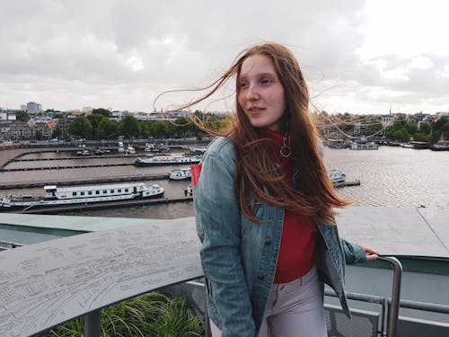 Woman Wearing Red Shirt and Blue Faded Denim Jacket and White Pants Looking at Side